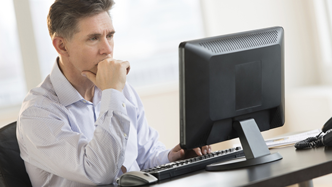 Mature businessman with hand on chin working on Desktop PC in office