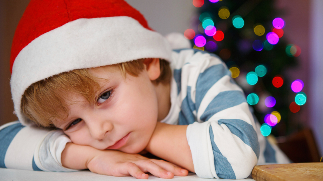 Little boy in santa hat with christmas tree and lights on background, dreaming