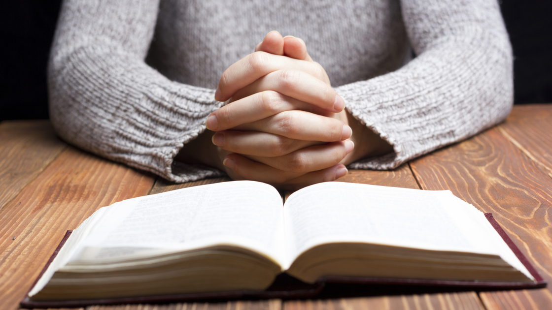 Woman hands praying with a bible in a dark over wooden table.