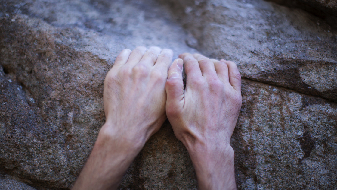 Man's hand hang onto rock while bouldering