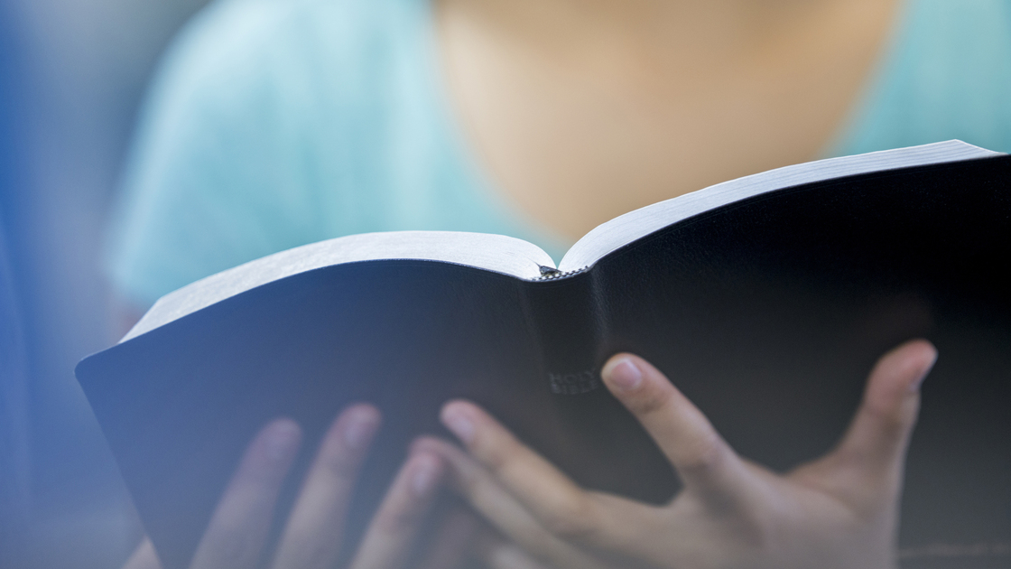A high school age girl is holding the Bible and is reading it with her fellow classmates during a Bible study.