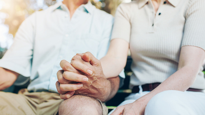 Cropped shot of mature couple holding hands while sitting together on a park bench. Focus on hands.