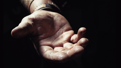Hand emerging from the dark. Wrist and the gentle open hand of a hardworking man extend from the darkness. The hand is faintly cupped and the fingers are pressed together. Background in soft focus.