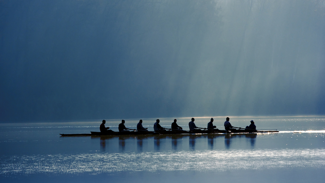 A canoe team rowing with power in order to win the competition. On background morning light through the forest. 