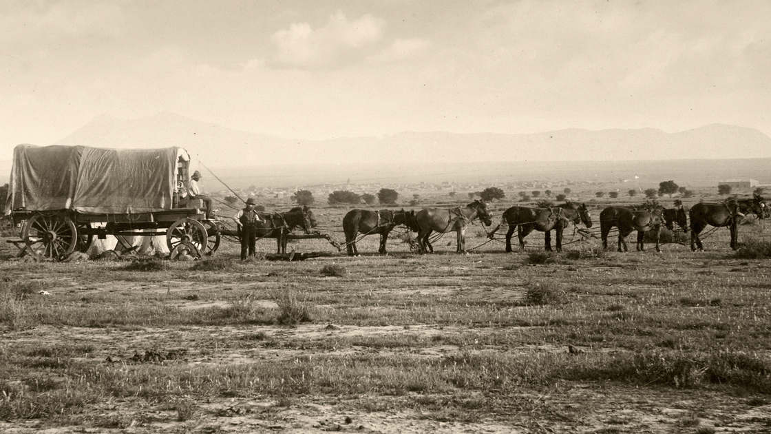 Vintage photograph of an old fashioned covered wagon pulled by a team of horses.