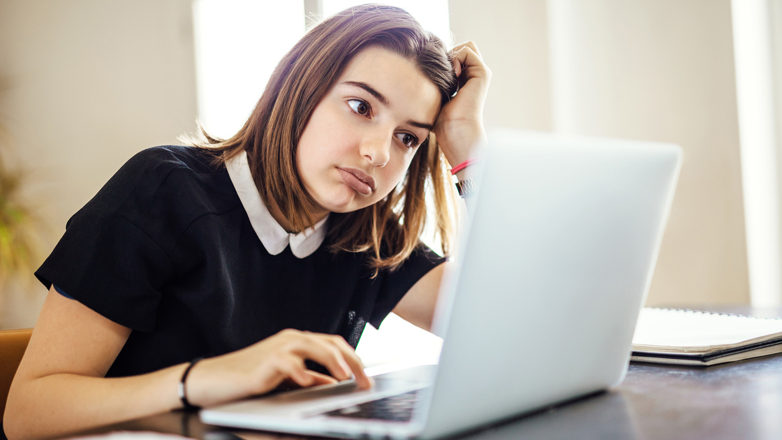 Frustrated youth using laptop computer trying to research something or finish homework on time while seated at desk with head resting on arm