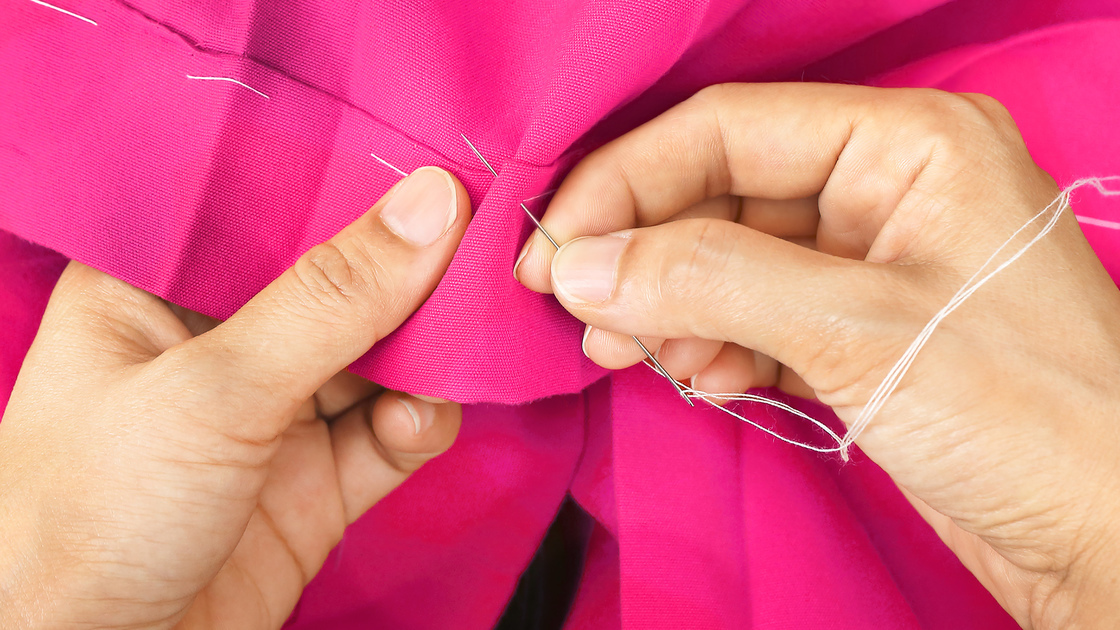 Hands sewing with a needle and thread.