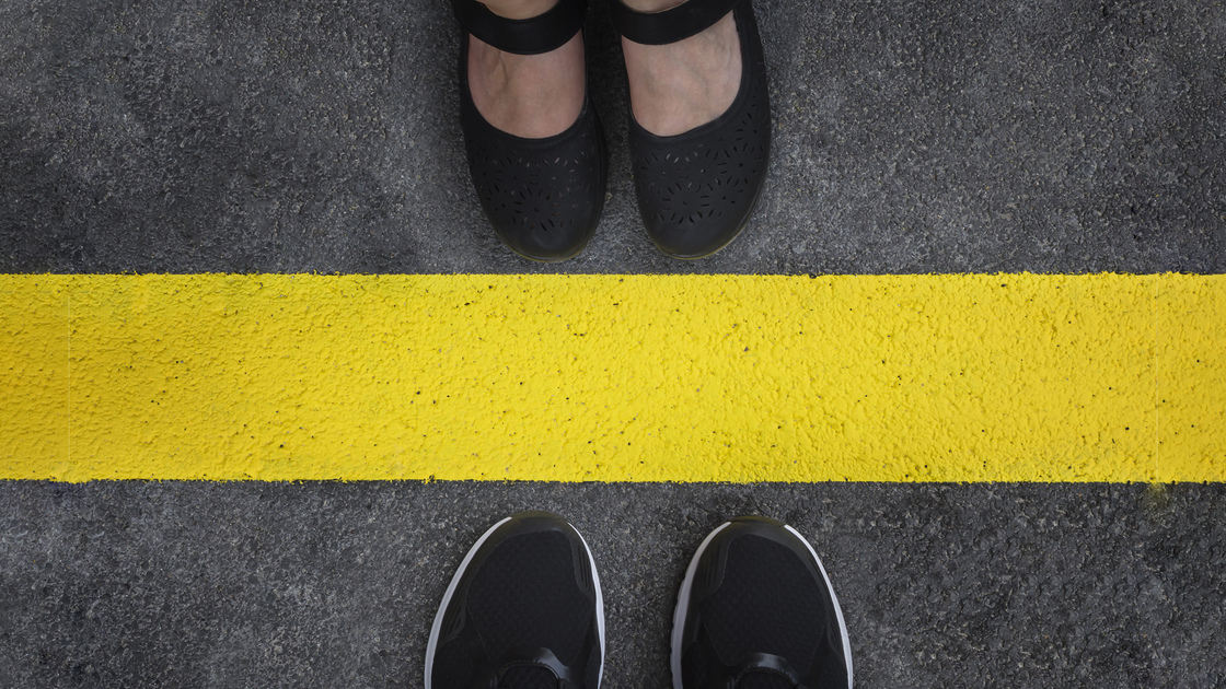 Legs of a couple standing opposite each other divided by the yellow asphalt line top view