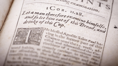 Detail of page from an ancient religious Christian text from the 1600s. Printed in old English language and typography. Shallow depth of field--focus on 1 Corinthians 11:28 scriptural reference.